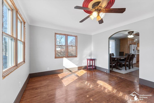 unfurnished room featuring arched walkways, a ceiling fan, baseboards, and hardwood / wood-style floors