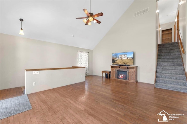 unfurnished living room featuring visible vents, high vaulted ceiling, a ceiling fan, a glass covered fireplace, and hardwood / wood-style floors