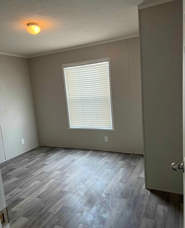 empty room featuring crown molding, wood finished floors, and a textured ceiling