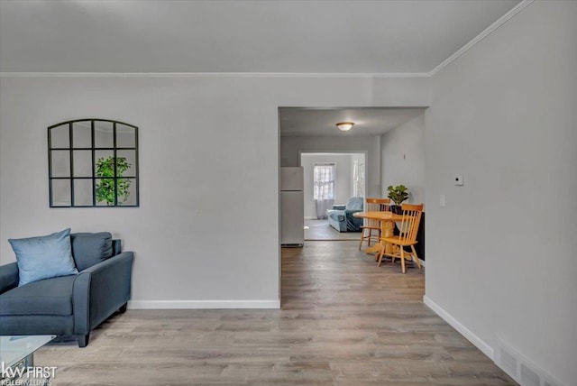 living room with light wood-type flooring, baseboards, visible vents, and ornamental molding