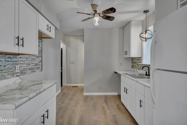 kitchen featuring baseboards, light wood-style floors, white cabinets, and freestanding refrigerator