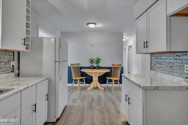 kitchen featuring light stone counters, white cabinets, light wood-style floors, and backsplash