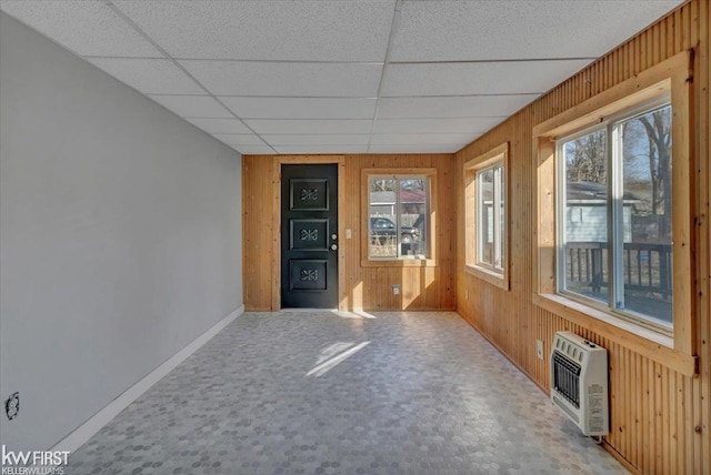 interior space with wooden walls, heating unit, baseboards, and a drop ceiling