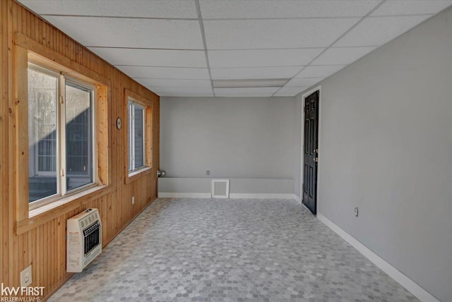 spare room with heating unit, a drop ceiling, wood walls, and carpet floors