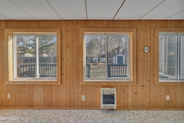 interior space featuring heating unit, a drop ceiling, wood walls, and carpet