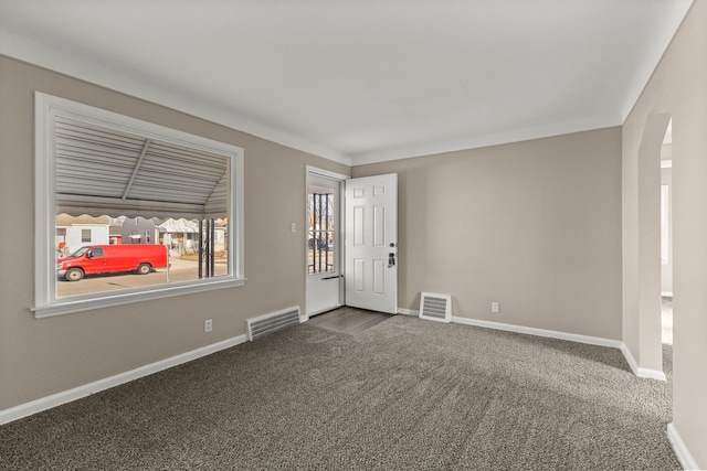 spare room featuring baseboards, visible vents, dark carpet, and arched walkways