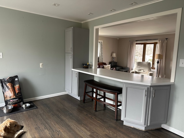 kitchen featuring a breakfast bar, dark wood-style floors, crown molding, light countertops, and baseboards