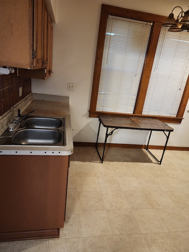 kitchen with brown cabinetry, backsplash, baseboards, and a sink