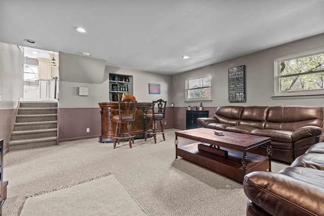 carpeted living area with recessed lighting, a wainscoted wall, a bar, and stairs