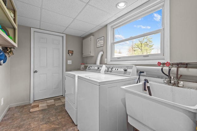 laundry area featuring baseboards, stone finish floor, washer and clothes dryer, a sink, and cabinet space