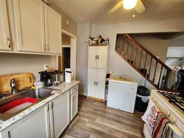 kitchen featuring light wood-type flooring, a ceiling fan, a sink, a textured ceiling, and white appliances