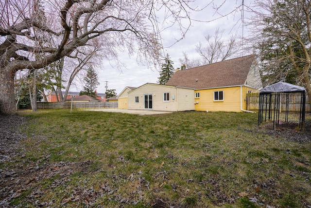 exterior space featuring a patio area, a lawn, a shingled roof, and fence