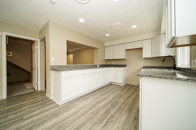 kitchen with recessed lighting, light wood-style flooring, dark stone countertops, white cabinets, and a sink