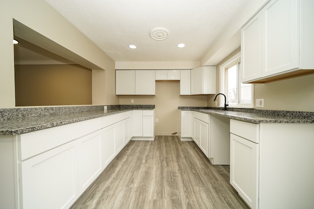 kitchen featuring dark stone counters, recessed lighting, light wood-style flooring, white cabinetry, and a sink