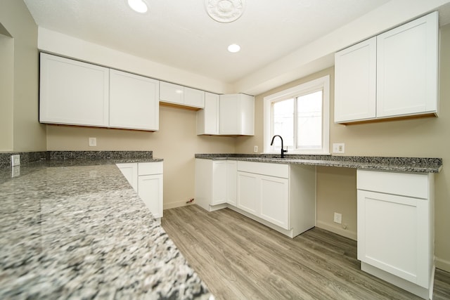 kitchen featuring recessed lighting, stone countertops, a sink, light wood-style floors, and white cabinetry