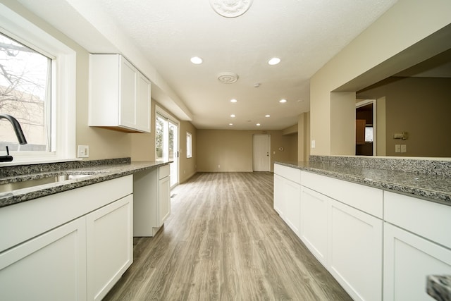 kitchen featuring light wood-type flooring, recessed lighting, dark stone countertops, white cabinetry, and a sink