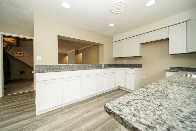 kitchen featuring recessed lighting, light wood-type flooring, light stone countertops, and white cabinetry