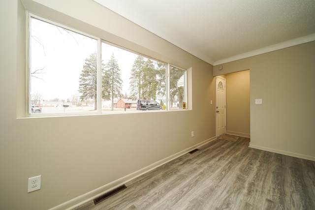 spare room featuring visible vents, a textured ceiling, baseboards, and wood finished floors