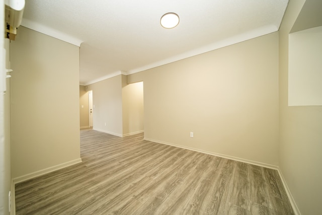 spare room with crown molding, baseboards, and light wood finished floors