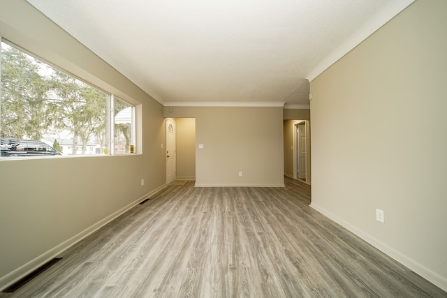 spare room featuring visible vents, light wood-style flooring, crown molding, and baseboards