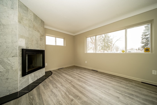 unfurnished living room featuring visible vents, baseboards, wood finished floors, and a tiled fireplace