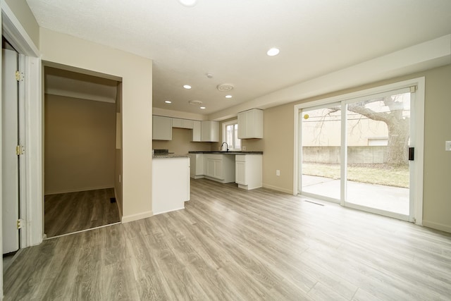 unfurnished living room featuring recessed lighting, light wood-type flooring, baseboards, and a sink