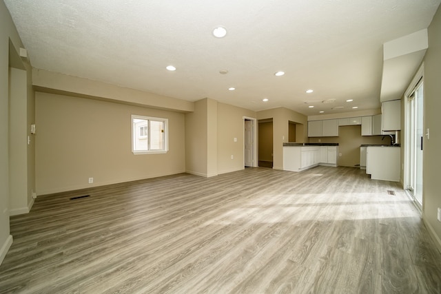 unfurnished living room featuring visible vents, recessed lighting, light wood-type flooring, and baseboards