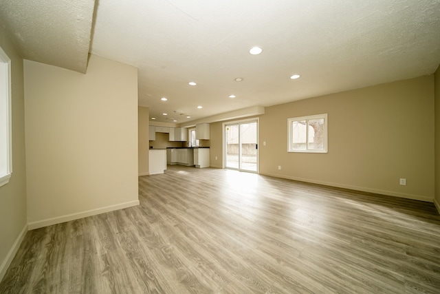 unfurnished living room featuring light wood-style flooring, recessed lighting, baseboards, and a textured ceiling