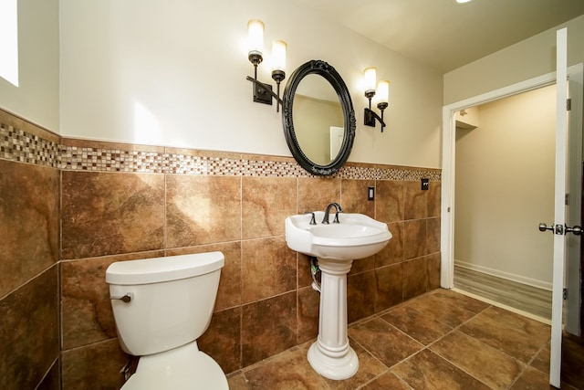 half bathroom with tile patterned floors, a wainscoted wall, toilet, and tile walls