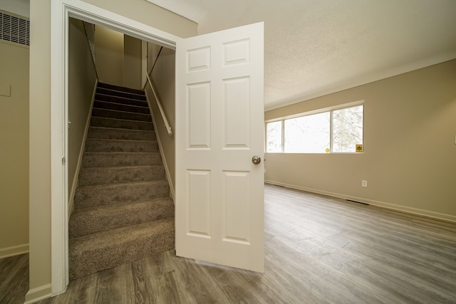 stairs with wood finished floors, baseboards, and a textured ceiling