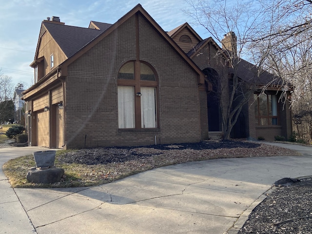 view of front of house featuring concrete driveway, an attached garage, brick siding, and a chimney