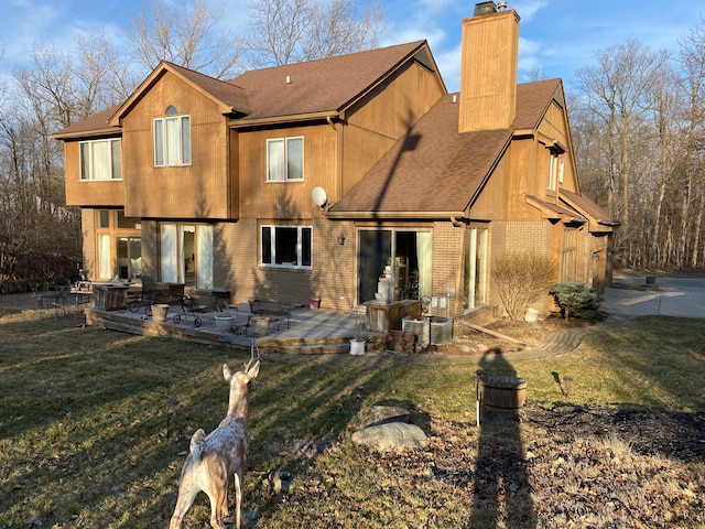 back of property featuring brick siding, roof with shingles, a chimney, a yard, and a patio