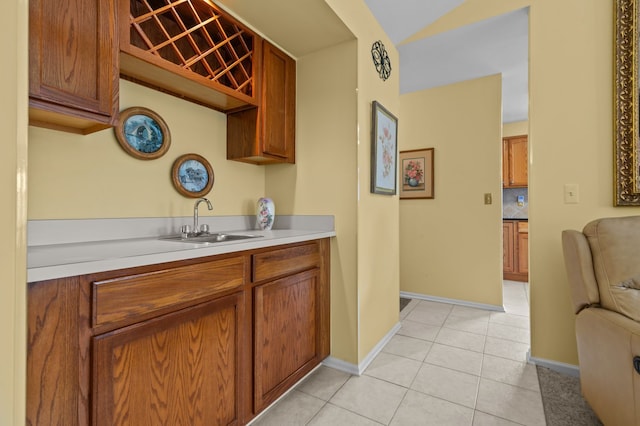kitchen featuring light tile patterned floors, a sink, brown cabinets, and baseboards