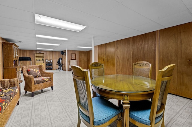 dining space featuring wood walls, a paneled ceiling, and light floors