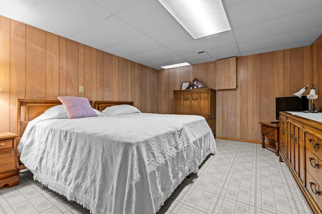 bedroom with wood walls, light floors, and a paneled ceiling