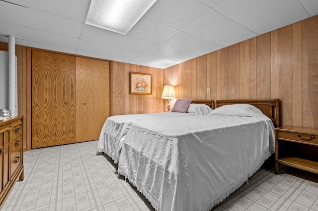 bedroom featuring light floors, wooden walls, and a drop ceiling