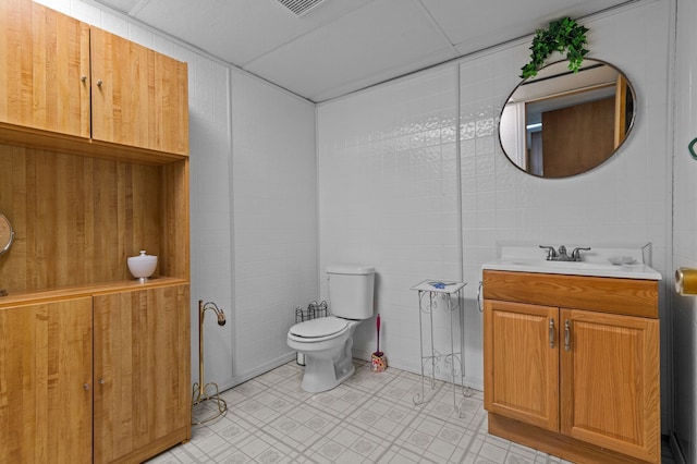 bathroom with toilet, tile patterned floors, tile walls, and vanity