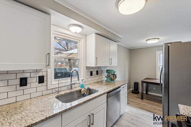 kitchen featuring light wood finished floors, a sink, stainless steel appliances, white cabinets, and crown molding