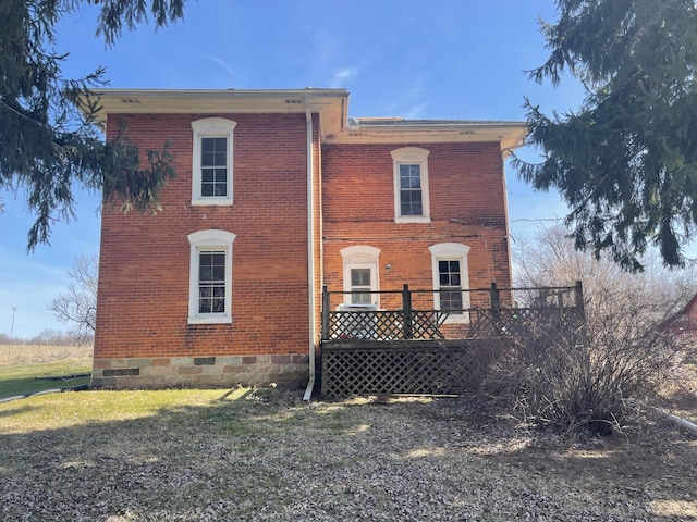 rear view of property with crawl space, a wooden deck, brick siding, and a lawn