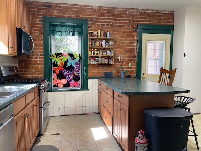 kitchen with dark countertops, brick wall, stainless steel appliances, and a peninsula