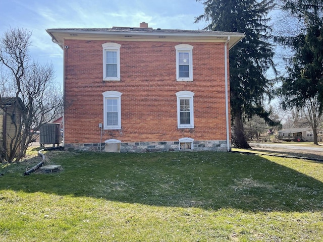 view of side of property with a yard, brick siding, and a chimney