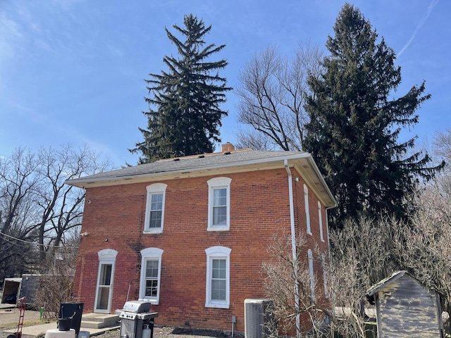 back of property with brick siding, a chimney, and central AC