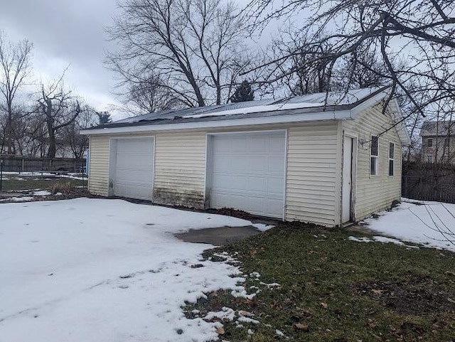 snow covered garage featuring a detached garage and fence