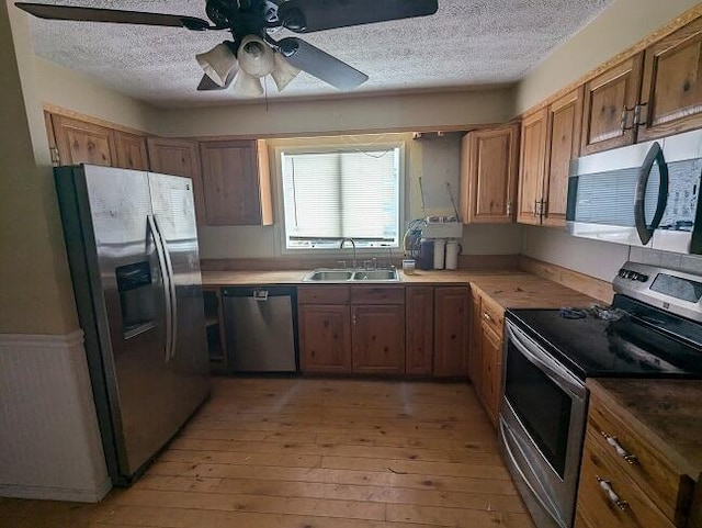 kitchen with light wood-type flooring, brown cabinets, a sink, stainless steel appliances, and ceiling fan