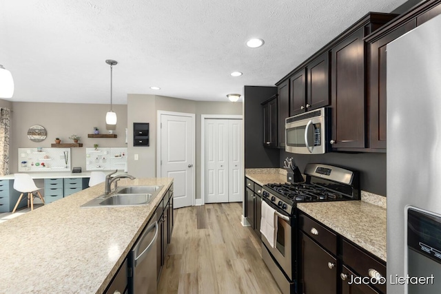 kitchen with light wood finished floors, a sink, light countertops, appliances with stainless steel finishes, and a textured ceiling