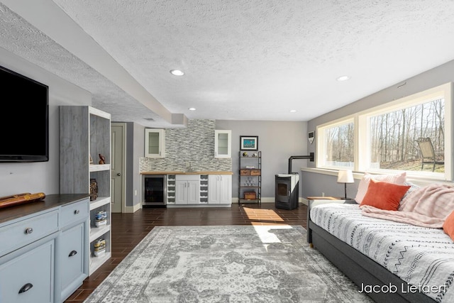 living area featuring a textured ceiling, a wood stove, baseboards, and wood finish floors