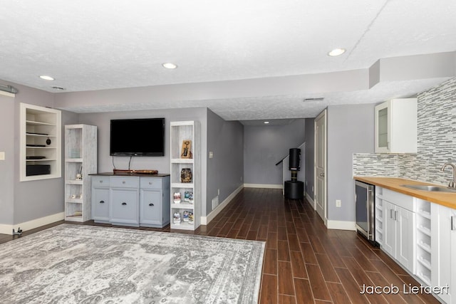 unfurnished living room featuring beverage cooler, baseboards, wood finish floors, a sink, and a textured ceiling