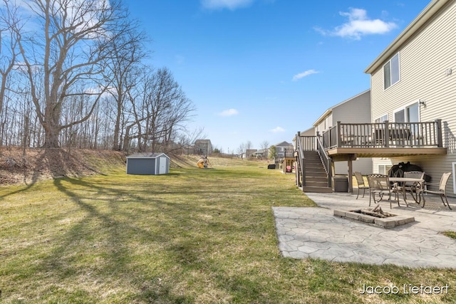 view of yard with an outbuilding, a wooden deck, a fire pit, a storage shed, and a patio area