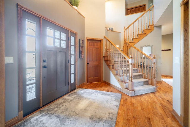 foyer entrance with stairway, wood finished floors, baseboards, and a towering ceiling