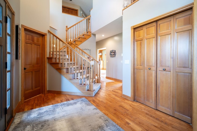 foyer entrance featuring stairway, baseboards, a high ceiling, and wood finished floors